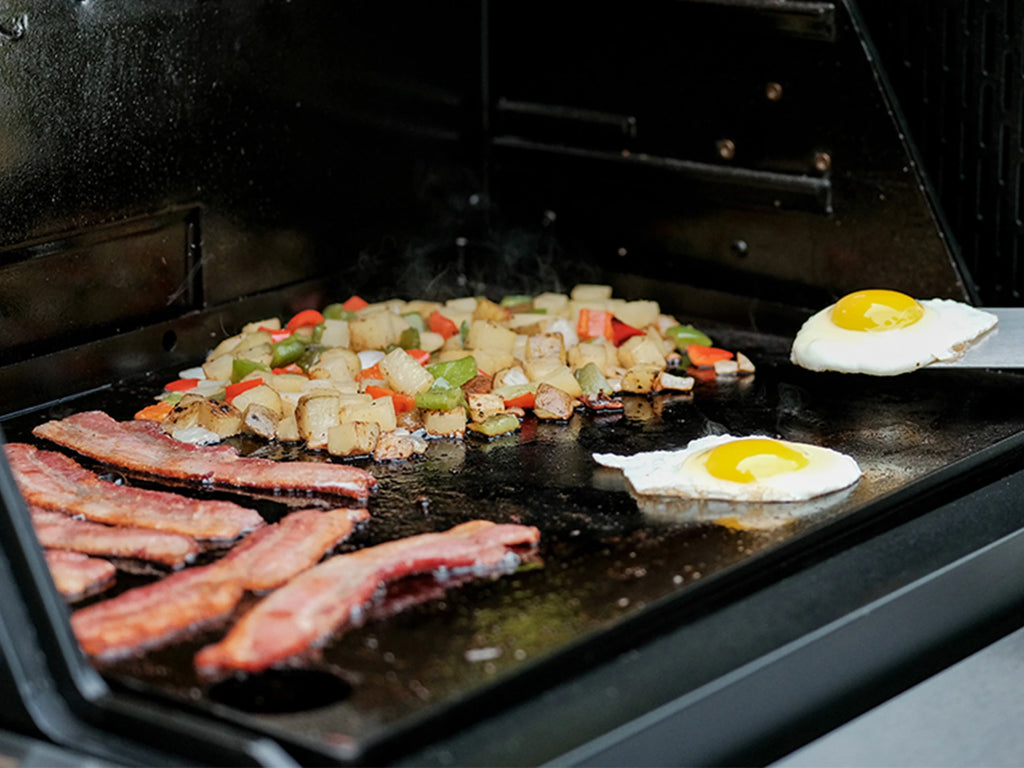 Breakfast cooking on a griddle. Includes eggs, bacon, and O'Brian hashbrowns.