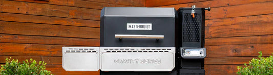 A Gravity Series 1150 Digital Charcoal Grill + Smoker sitting outside in front of a wooden wall. The left side shelf is up, and the front folding shelf is down. The charcoal hopper and control panel are mounted on the right side.