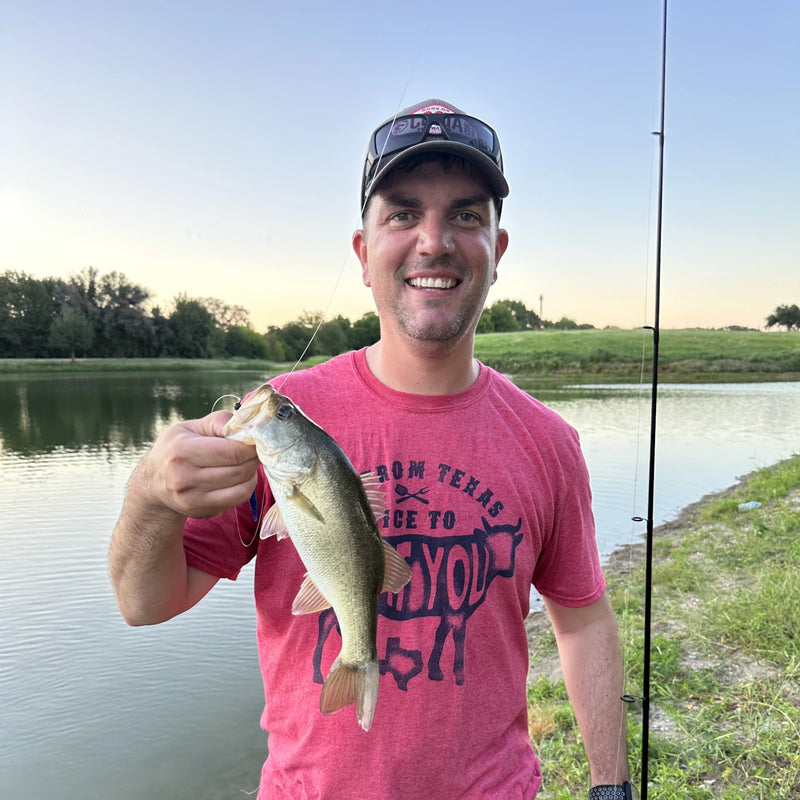 Tim Hoff standing near a canal holding a fishing rod in one hand and and a fish in the other.