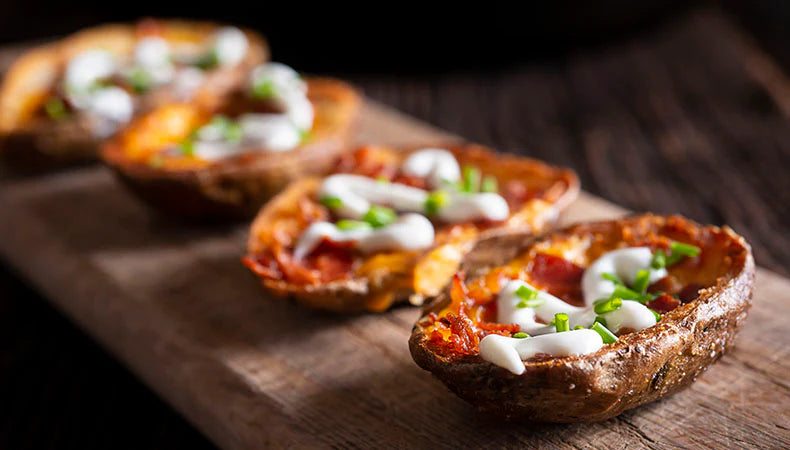 A row of twice-backed potatoes in a row on a board. The potatoes are topped with chopped bacon, sour cream, and chopped chives.