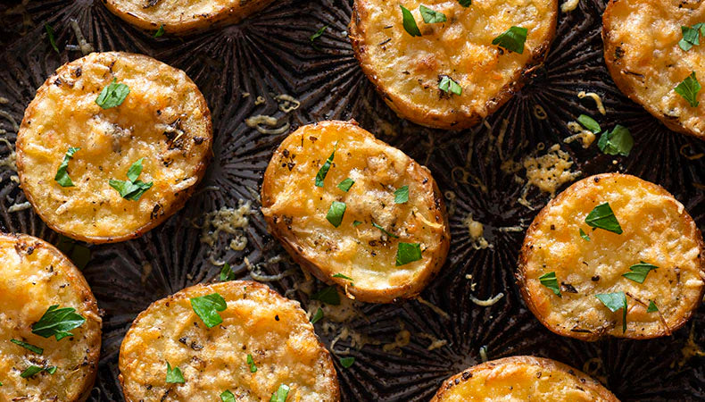 Grilled potato slices sprinkles with fresh herbs sit on a serving platter.