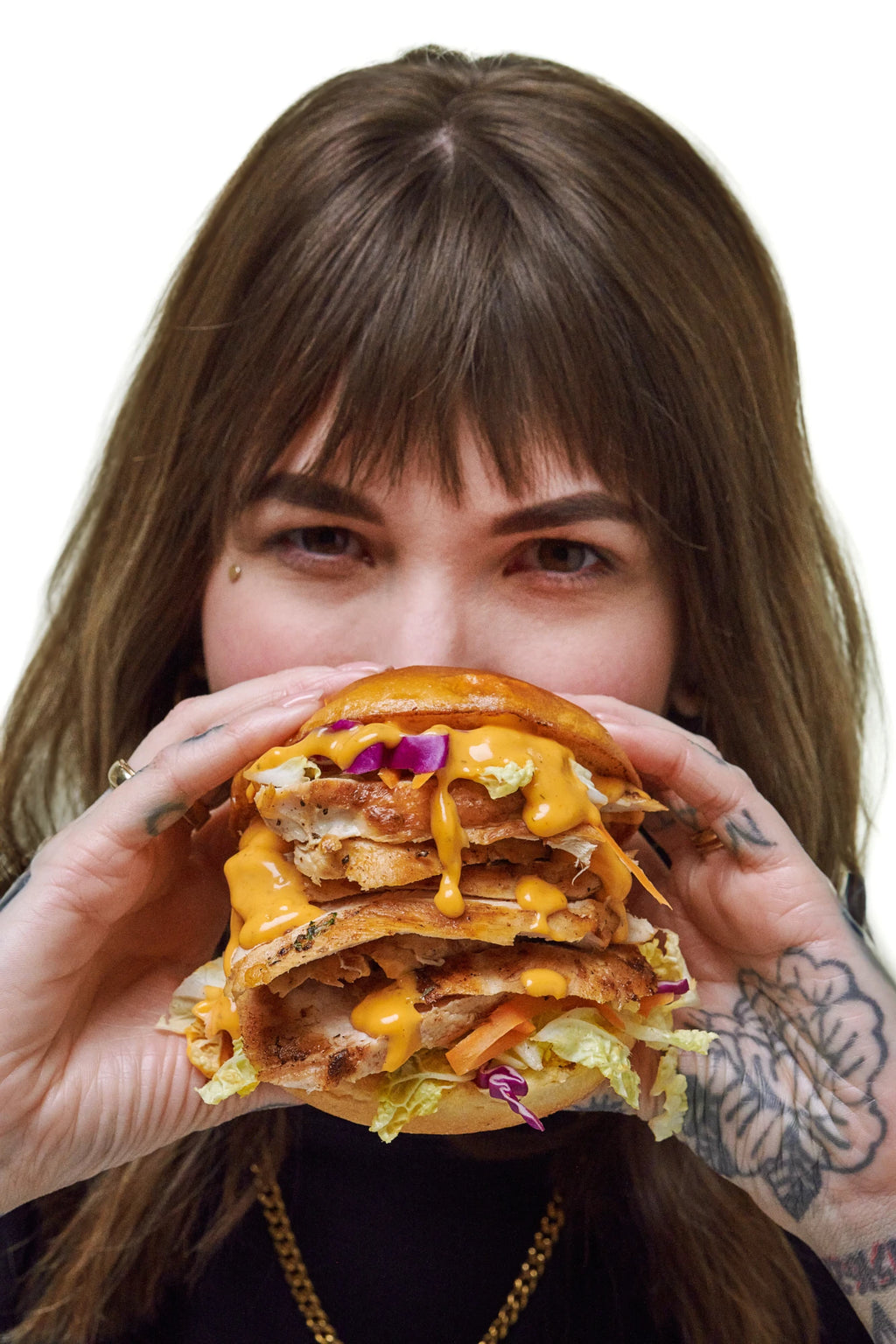 A woman holds an overstuffed sandwich on a burger bun in front of her face