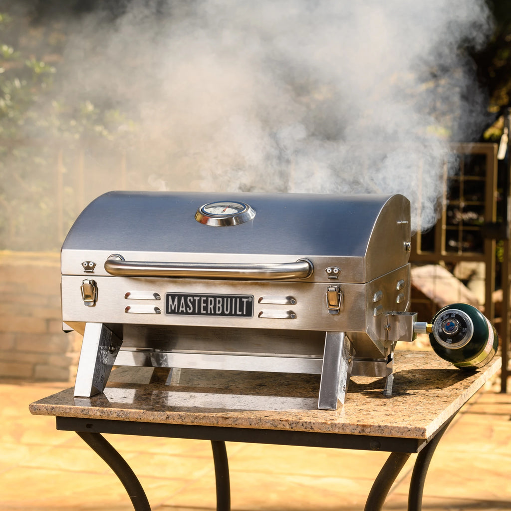Smoke escapes from a closed grill as it sits on a marble-topped table. A one-pound gas cylinder is connected to the valve on the right. The cylinder is at an angle and the bottom rests on the table.