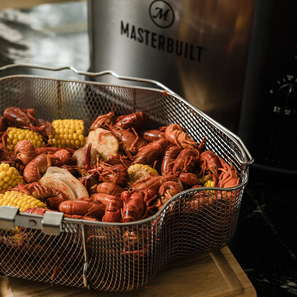 A fryer basket full of a steamed low country boil including crawfish, chunks of corn on the cob, onions, and potatoes