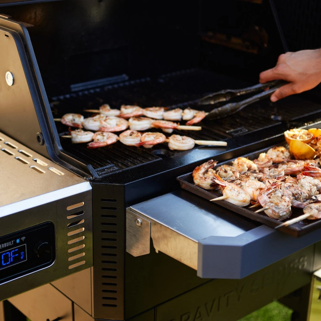 Someone uses tongs to remove shrimp skewers from the grill and place them on a serving platter resting on the front shelf of a Gravity Series grill