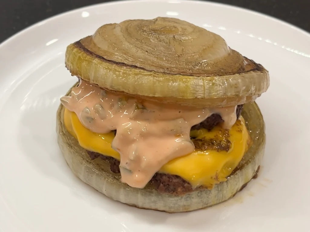 A burger topped with melted cheese and spicy sauce, sandwiched between 2 grilled onion slices.